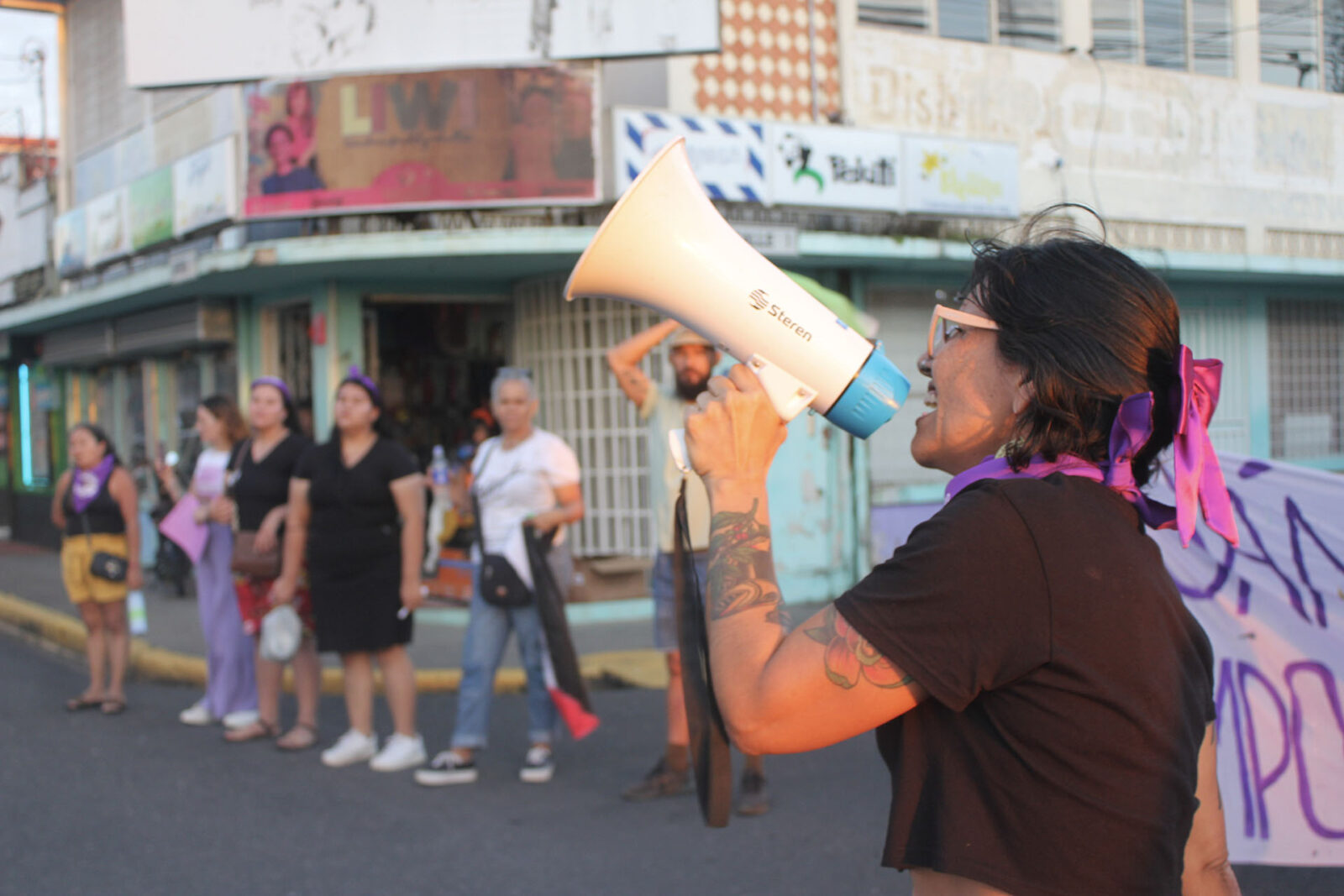 Alt text: a woman with a pink ribbon in her hair holding a megaphone.