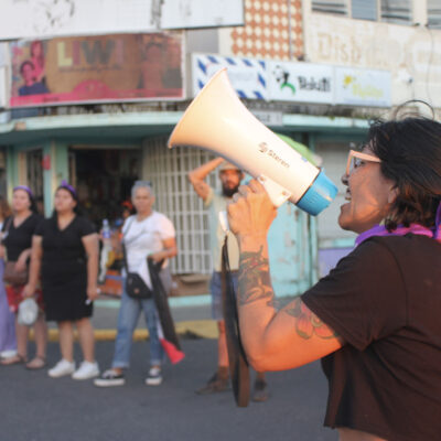 Alt text: a woman with a pink ribbon in her hair holding a megaphone.